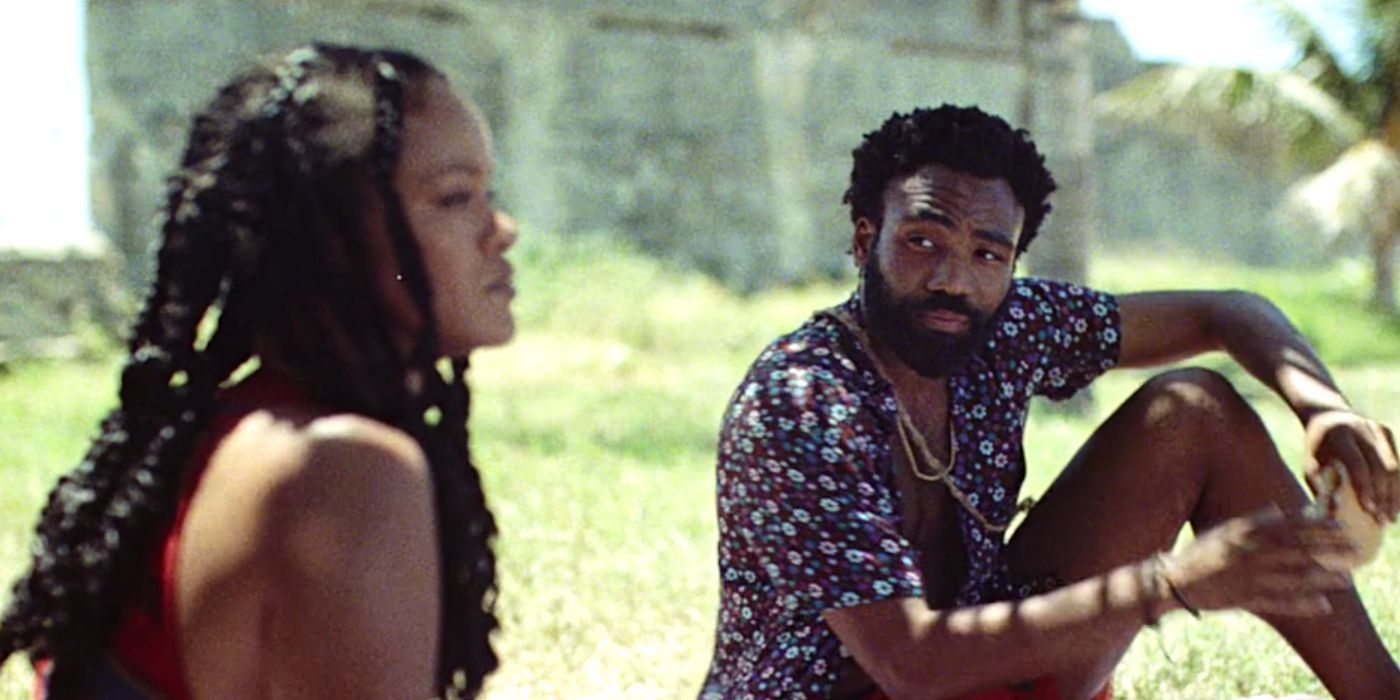 Donald Glover and Rihanna sitting in the grass in Guava Island