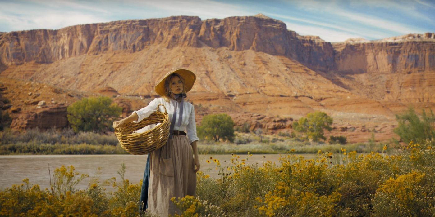 Sienna Miller sostiene una canasta en un campo de hierba junto a un río en Horizon: An American Saga.