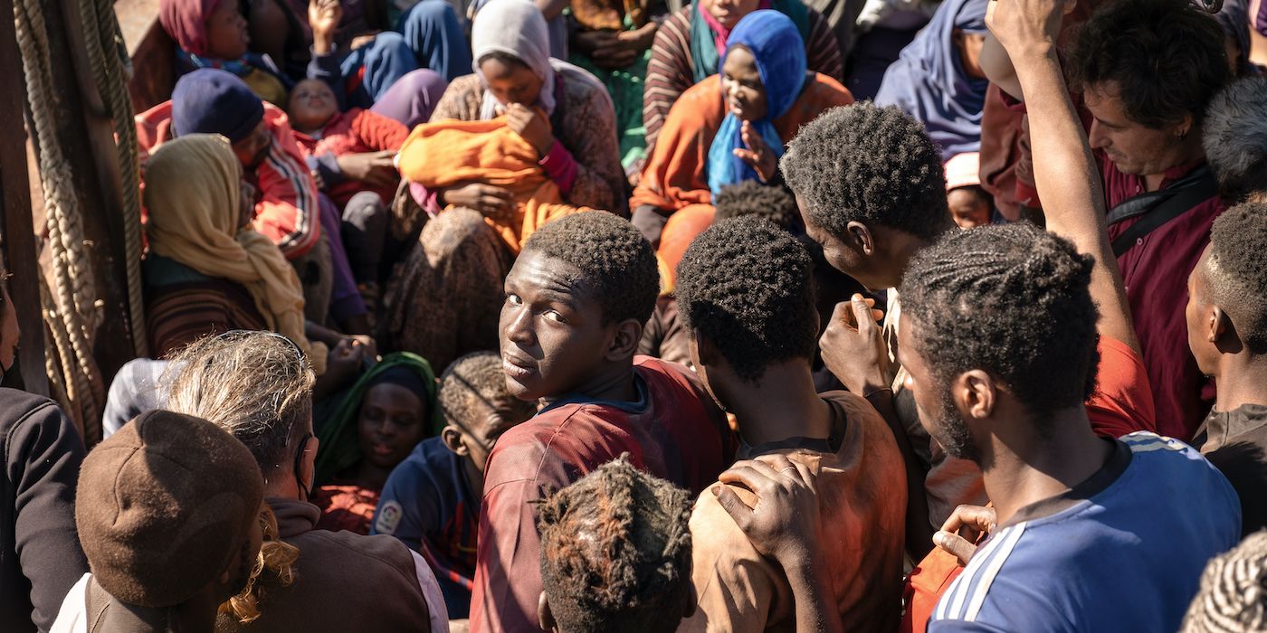 Seydou stands in the middle of a crowded group while looking back towards the camera in a still from Io Capitano. 