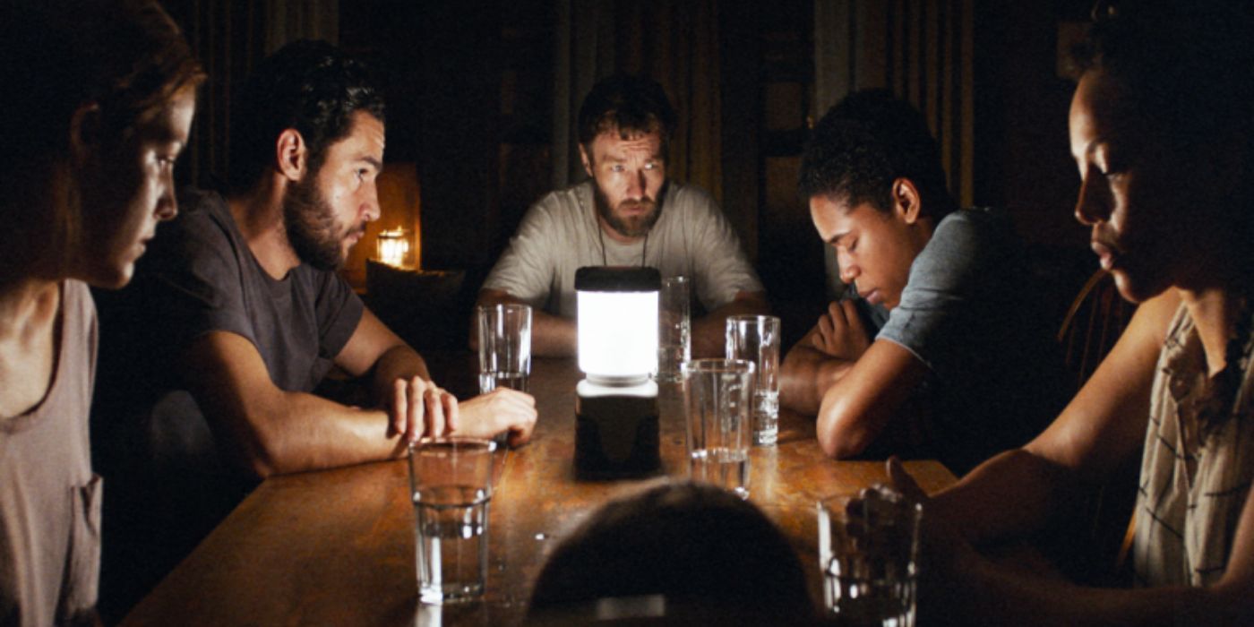 the survivors gather around a table with a single lamp in the middle