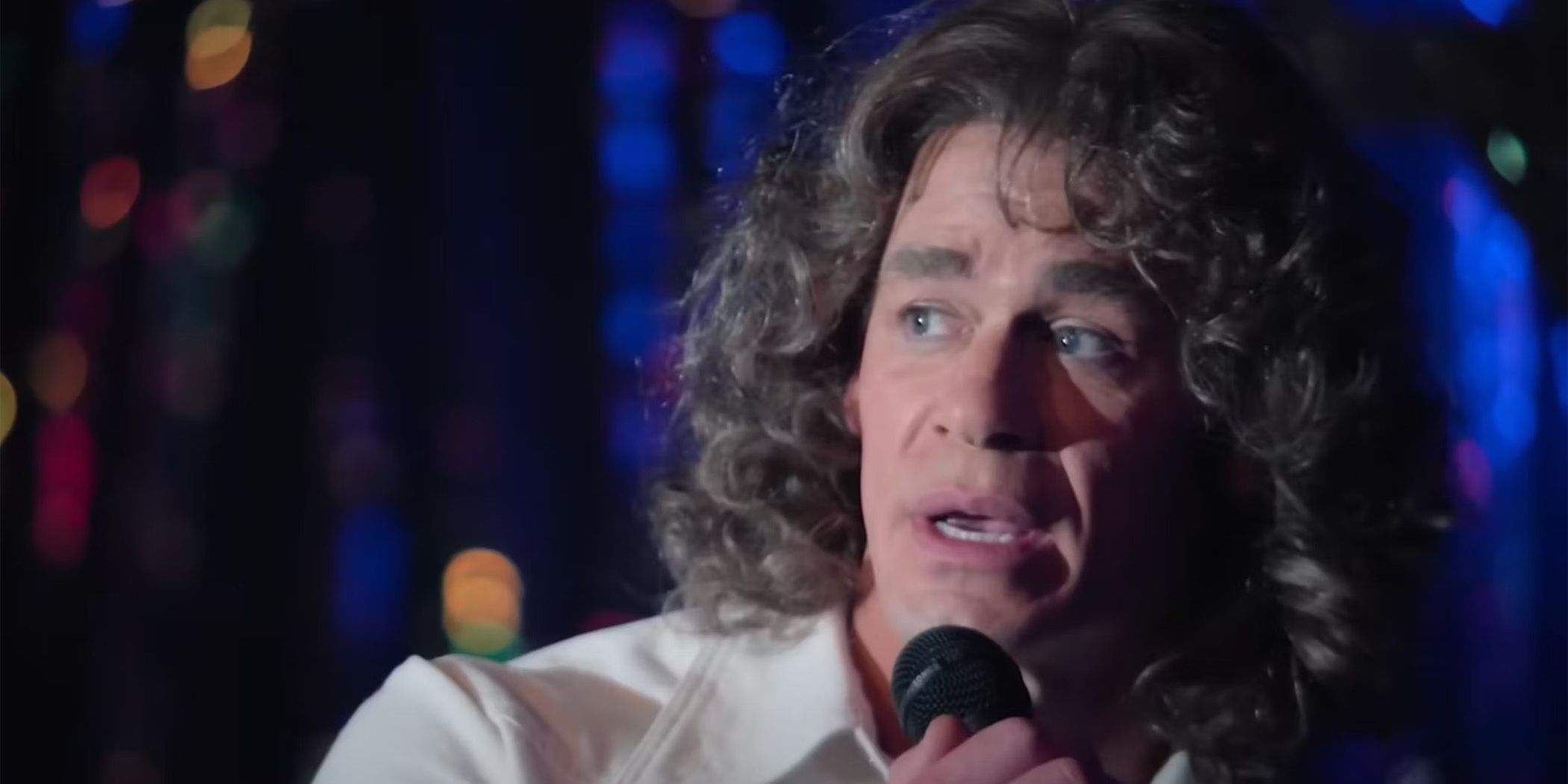 John Cena in curly grey wig singing on a stage in Ricky Stanicky
