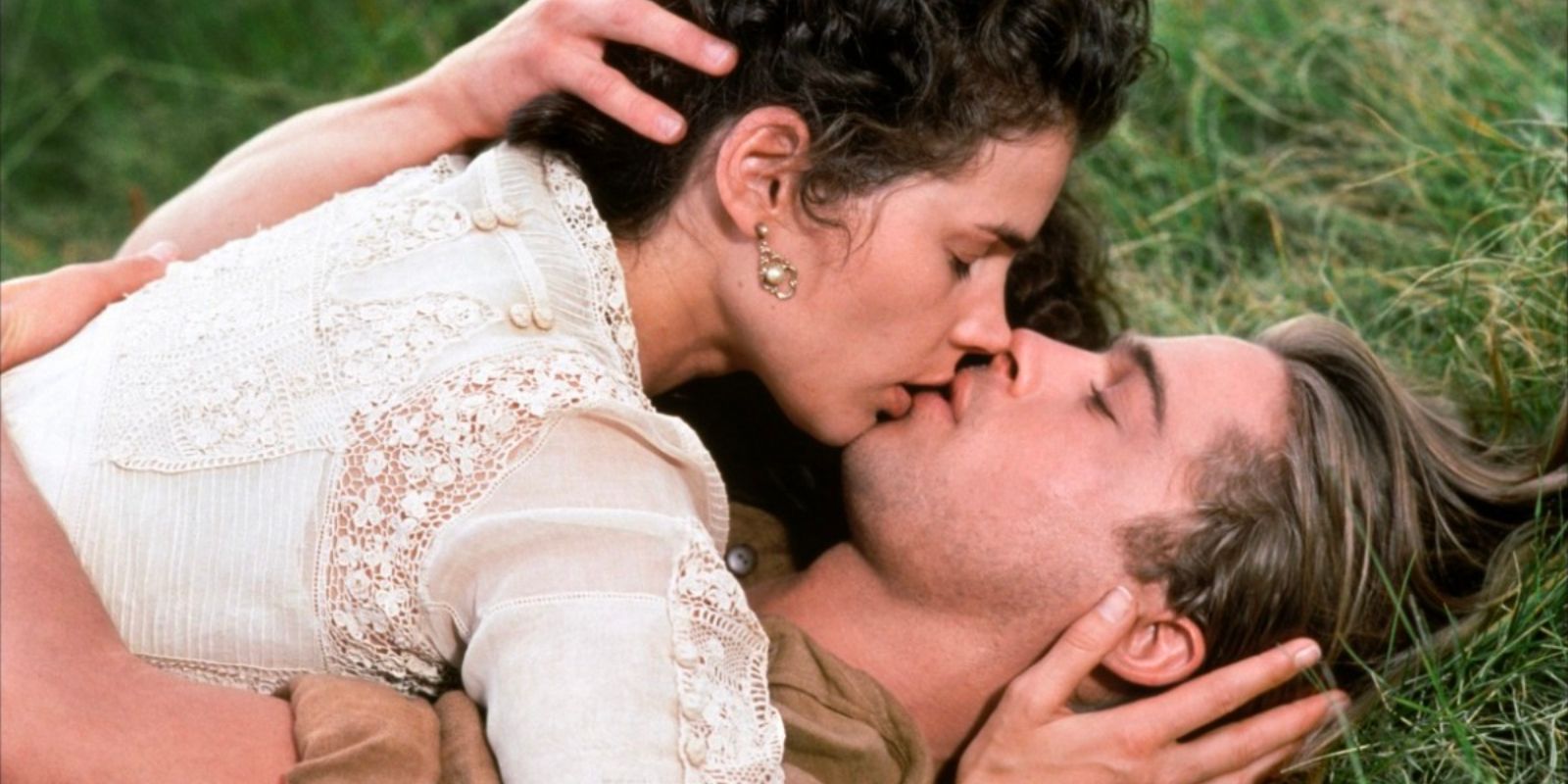 A woman lies on top of a man, the two passionately kissing as they lie on the grass.