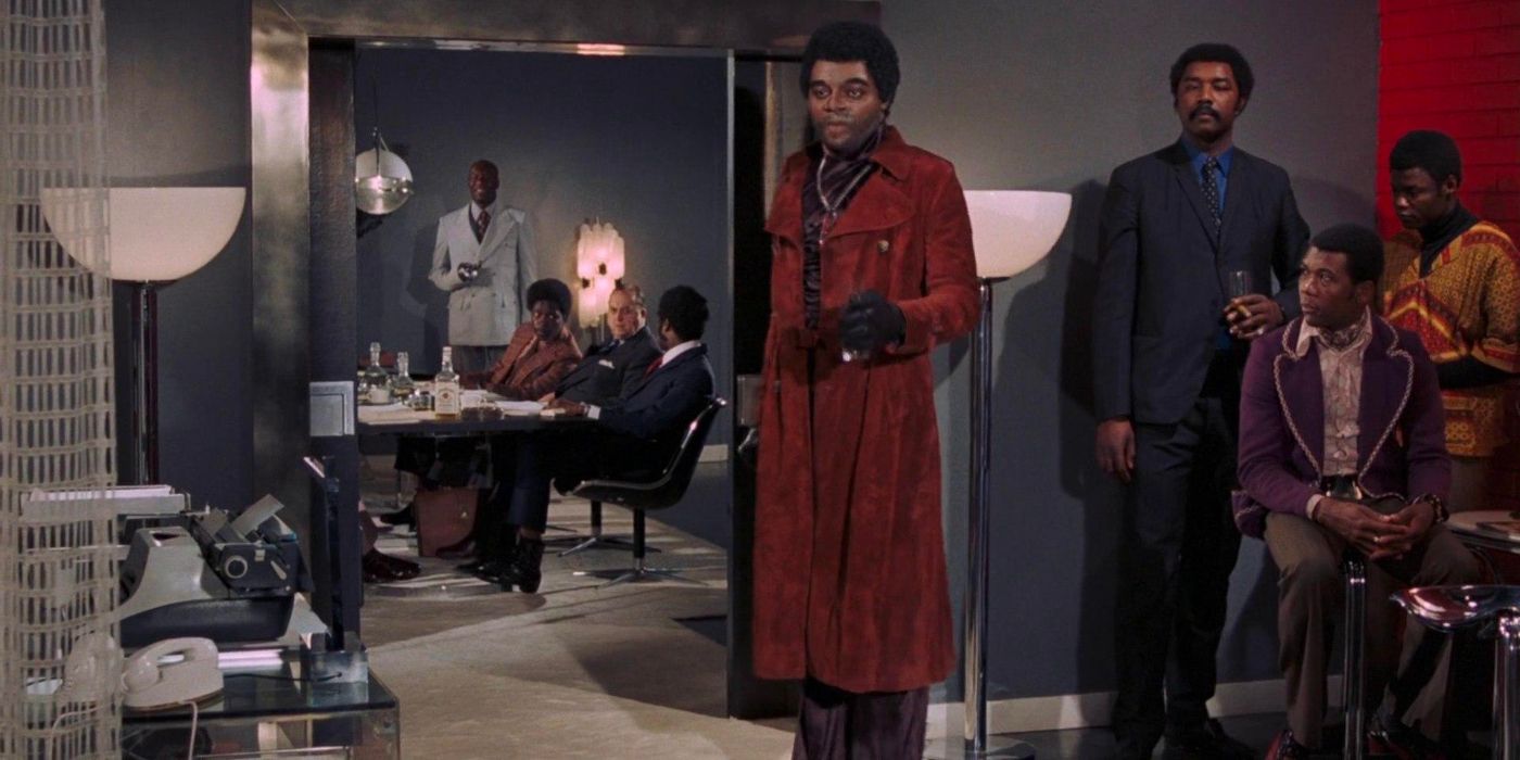 Mr. Big (Yaphet Kotto) stands in his club with a drink in hand, wearing a red coat as he orders James Bond's death.