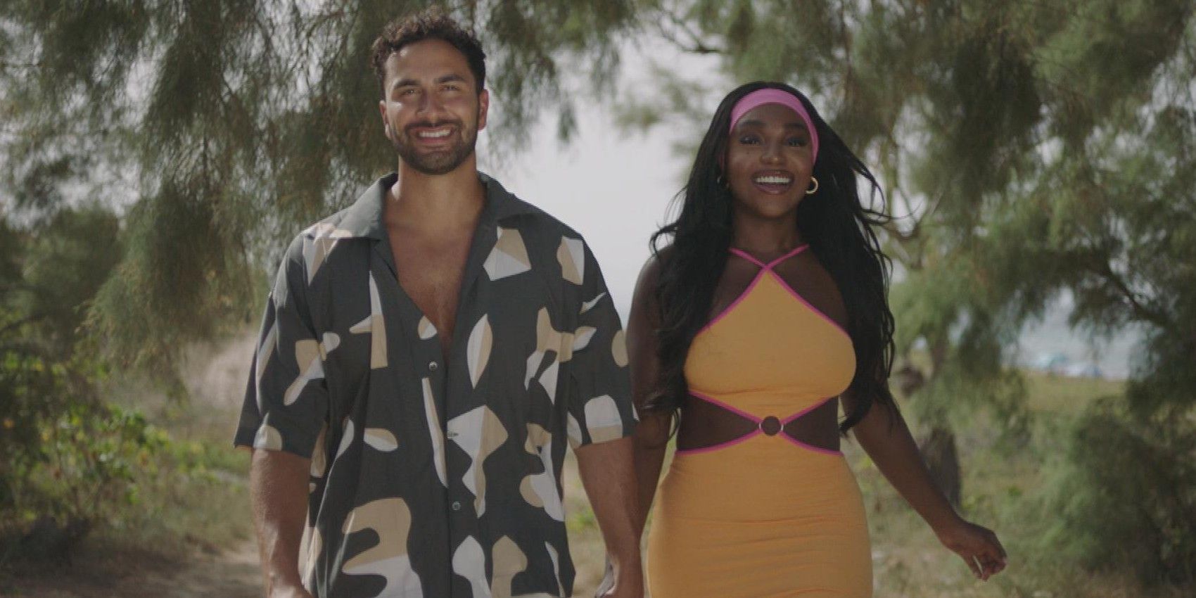 Lochan & Whitney hold hands and smile while walking through foliage in Love Island UK