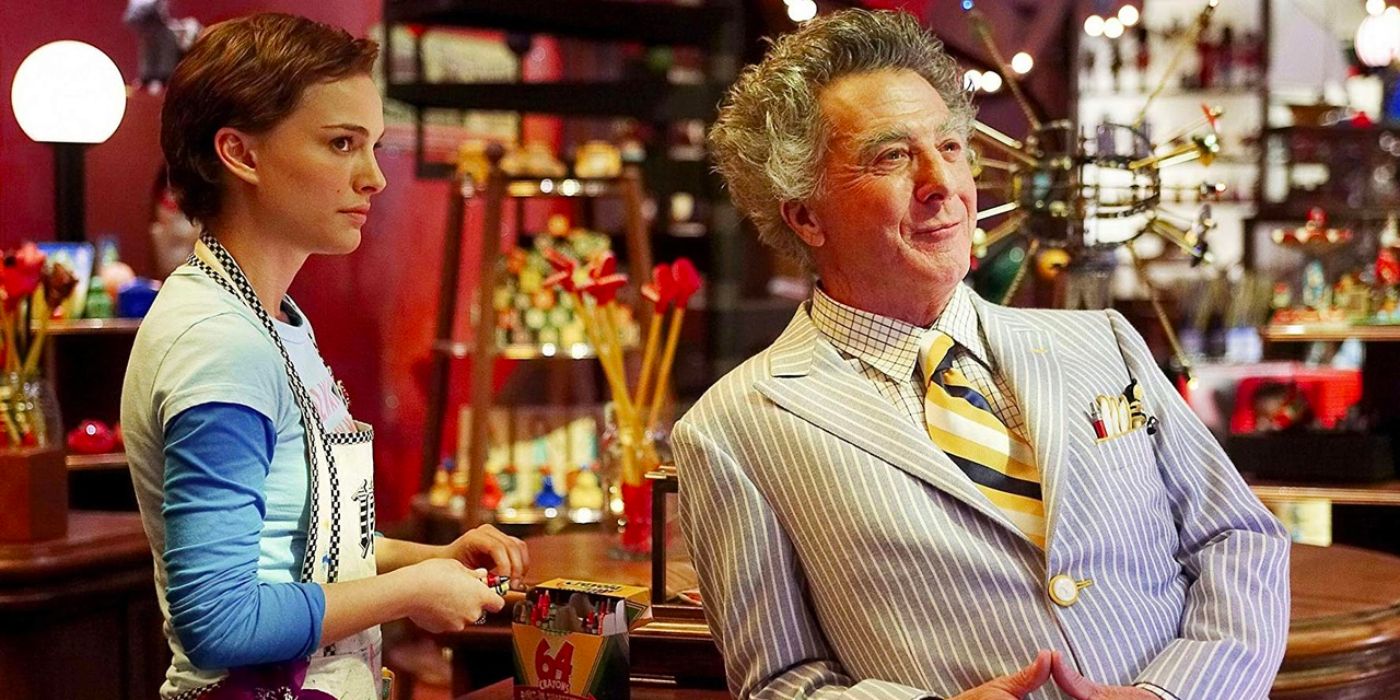 A smartly dressed and eccentric man leans back on the counter while a store clerk potters behind him. 