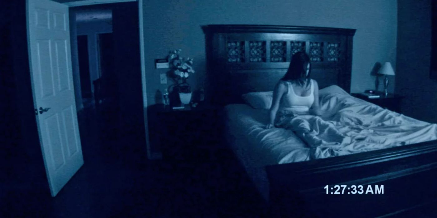 A nighttime camera captures a woman sitting in bed in Paranormal Activity