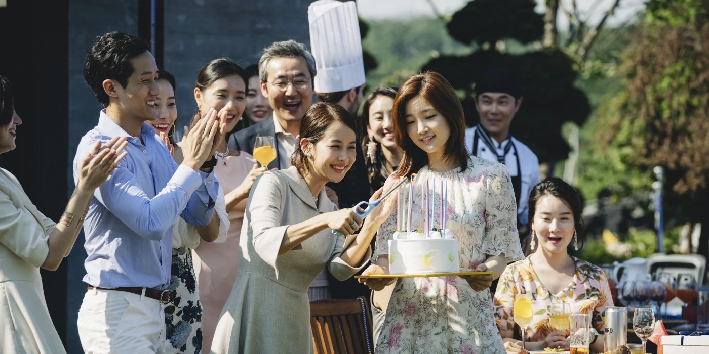 Cho Yeo-jeong as Choi Yeon-gyo, smiling and lighting candles on a birthday cake held by Park So-dam as Kim Ki-jung, while a crowd applauds in Parasite