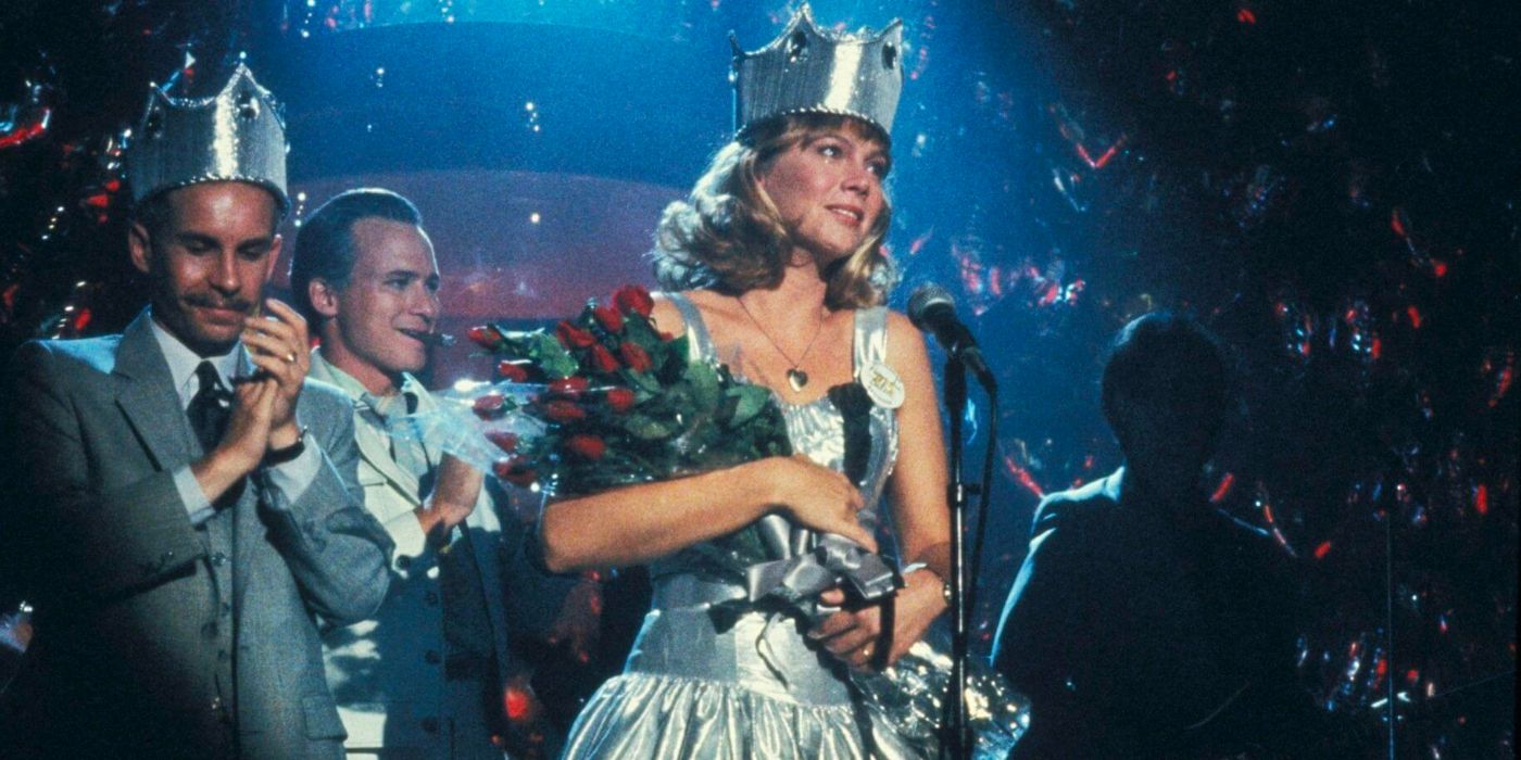 A woman is standing on stage, wearing a crown, holding a bouquet of roses and speaking into a microphone.