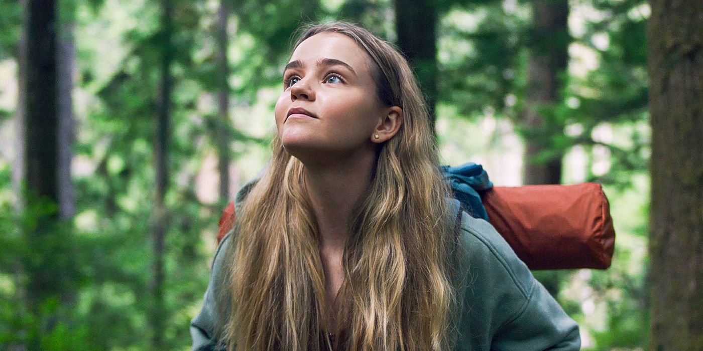Megan Stott as Penelope looking up a towering tree in the forest while wearing a backpack with a sleeping pad Penelope