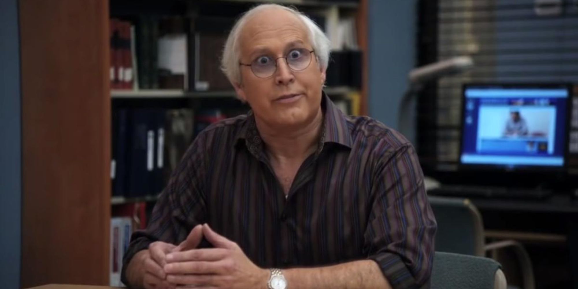 Pierce Hawthorne (Chevy Chase) from Community sitting in the study room with his hands folded on the table