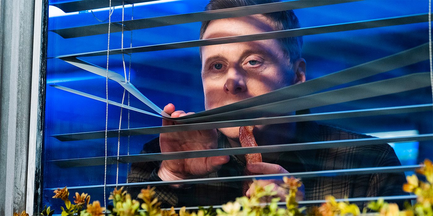 Alan Tudyk as Harry in Resident Alien peeking out some blinds