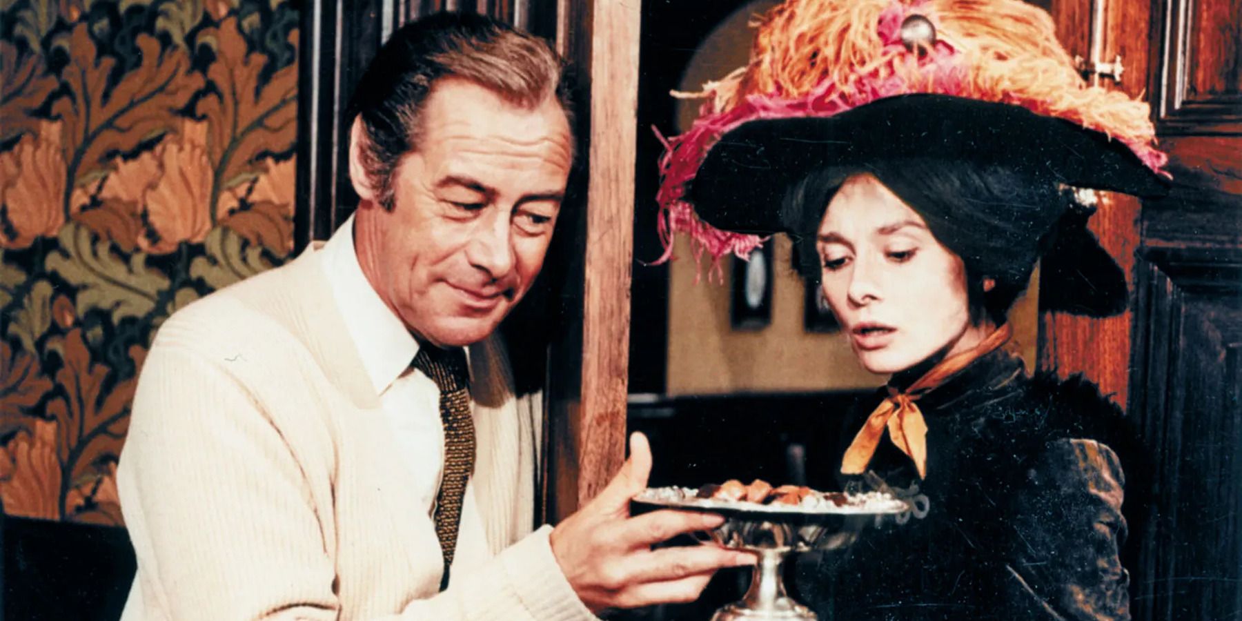 a man in a suit offering a woman with a big hat a tray with food