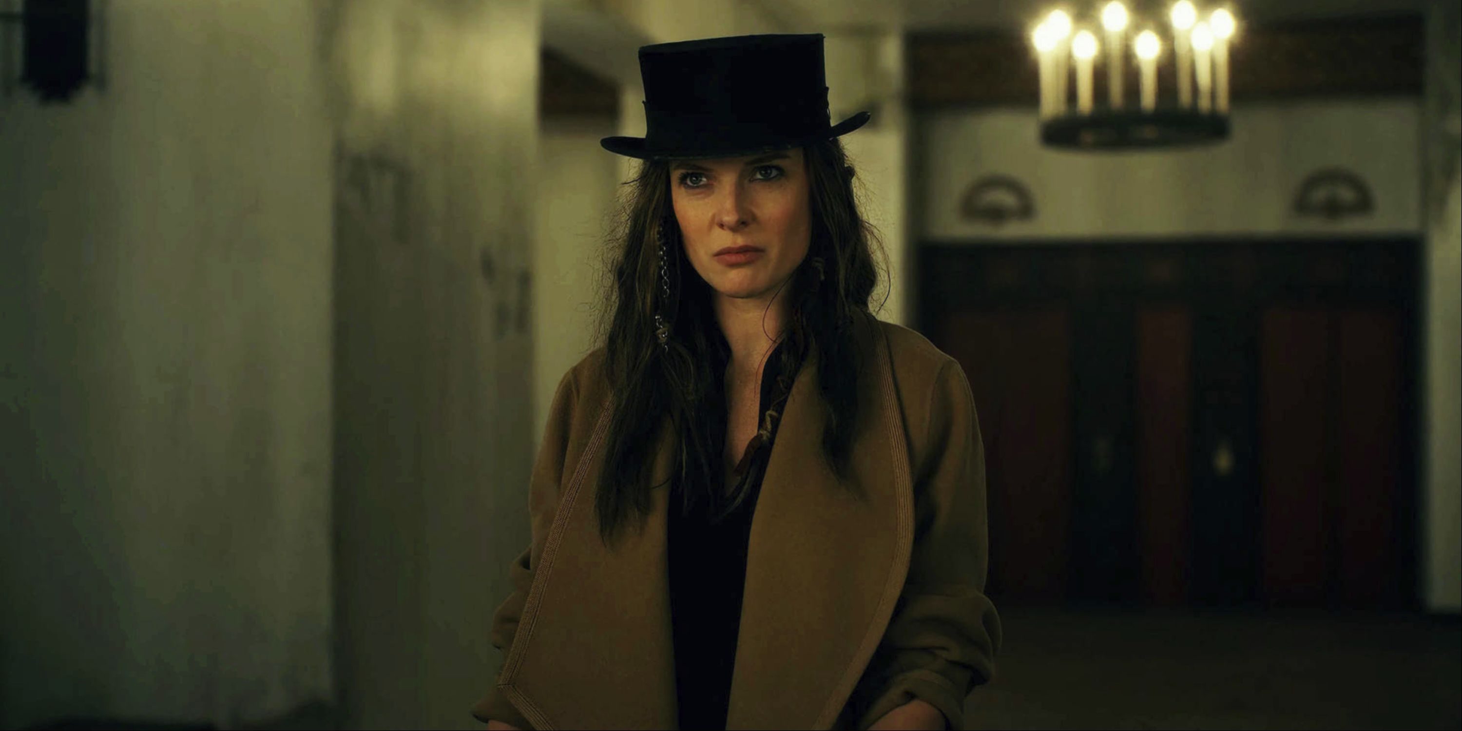 Rebecca Ferguson as Rose the Hat, standing in a dimly lit hallway wearing a brown coat and black top hat in Doctor Sleep