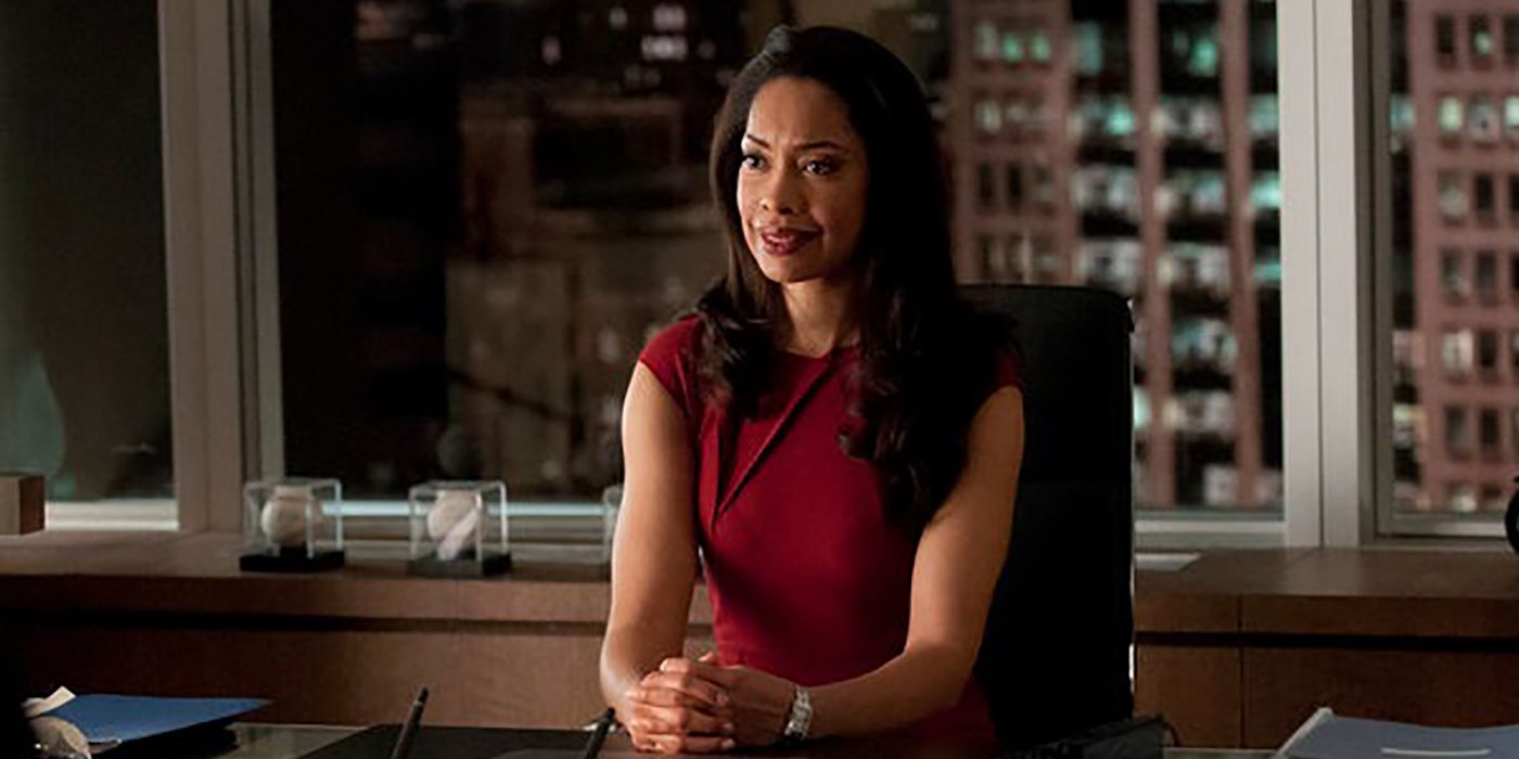 Jessica Pearson sitting behind her desk smiling, arms clutched in front of her on Suits.