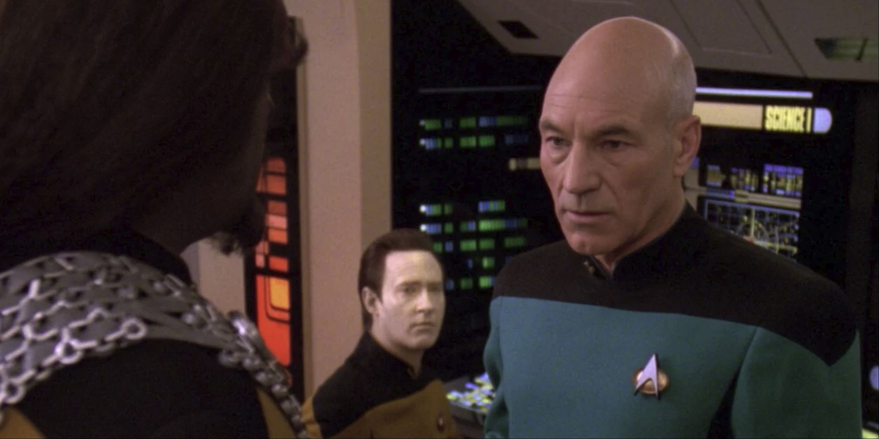 Patrick Stewart as Jean-Luc Picard in conversation with Michael Dorn as Worf with Brent Spiner as Data in the background in Star Trek: The Next Generation