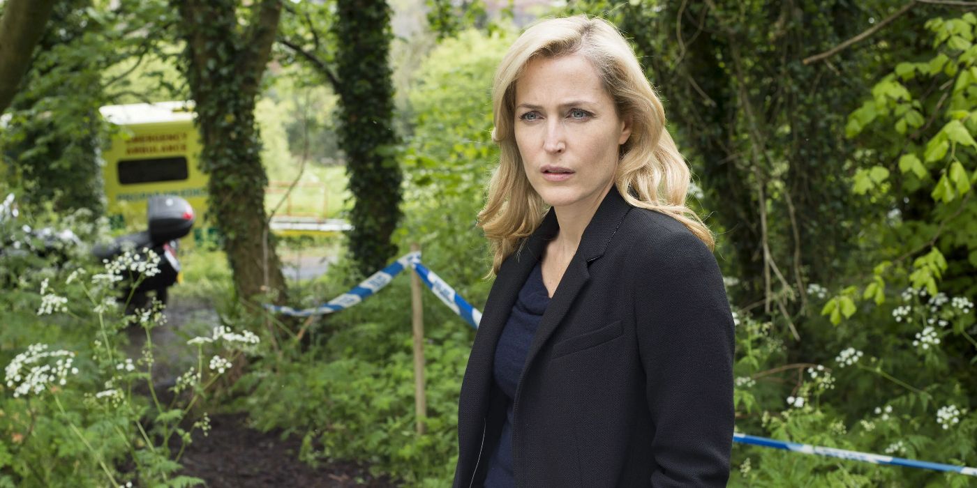 Gillian Anderson as Stella Gibson wearing a black jacket and navy blouse, standing in a country area and looking to the right in The Fall
