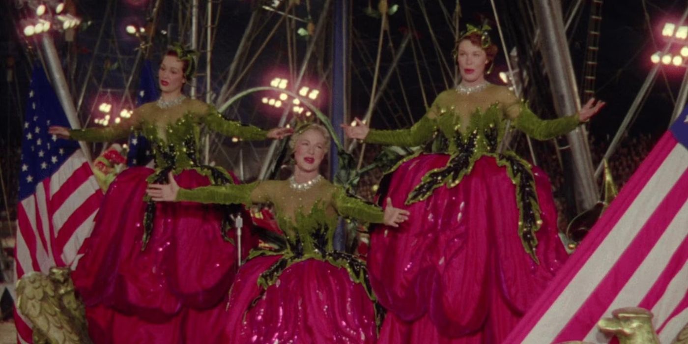 Three dancers in green and pink dresses, performing with their arms outstretched in The Greatest Show on Earth