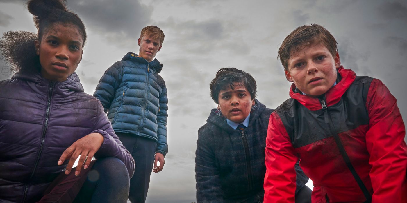 Four dirtied kids pressed up warm look down at the camera as clouds hand low in the sky behind them.