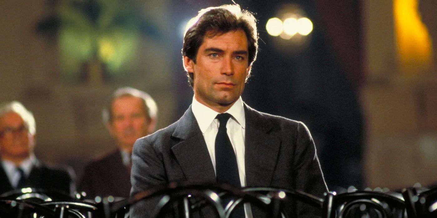 James Bond (Timothy Dalton) sits alone in a hall wearing a dark suit.