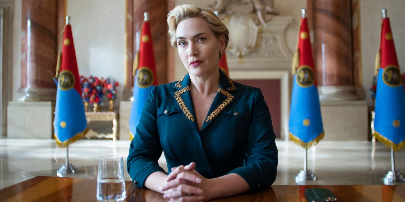 Kate Winslet sitting at a table with hands clasped in The Regime