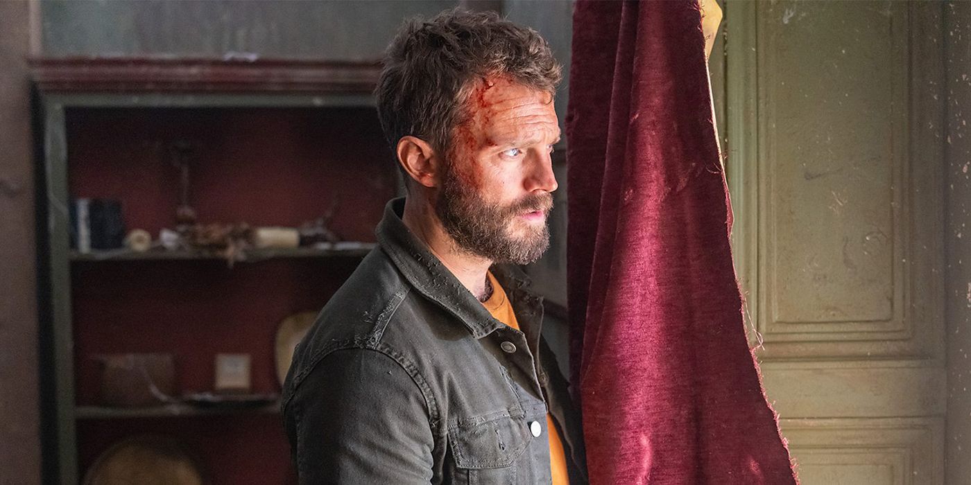 A man (Jamie Dornan) looks out a window while the side of his face is bloodied for a scene in The Tourist Season 2.