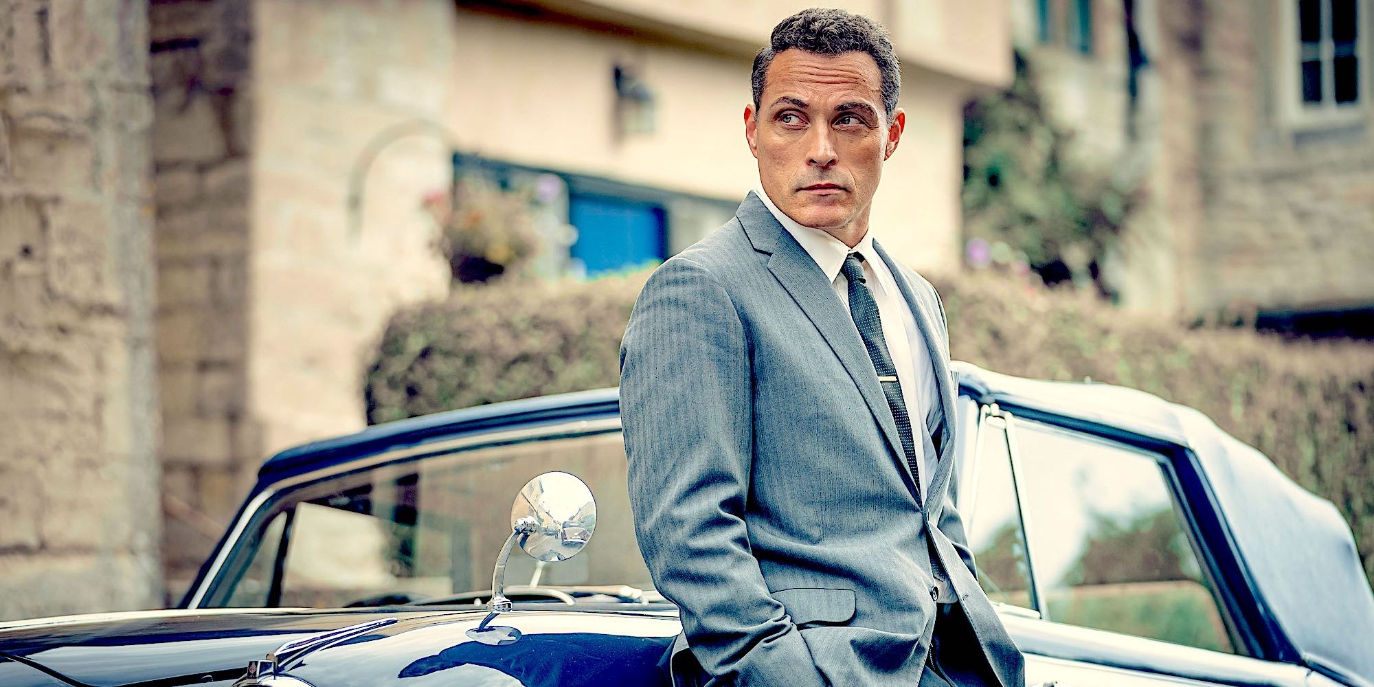 Rufus Sewell as Mark Easterbrook, wearing a suit and leaning against a car in The Pale Horse
