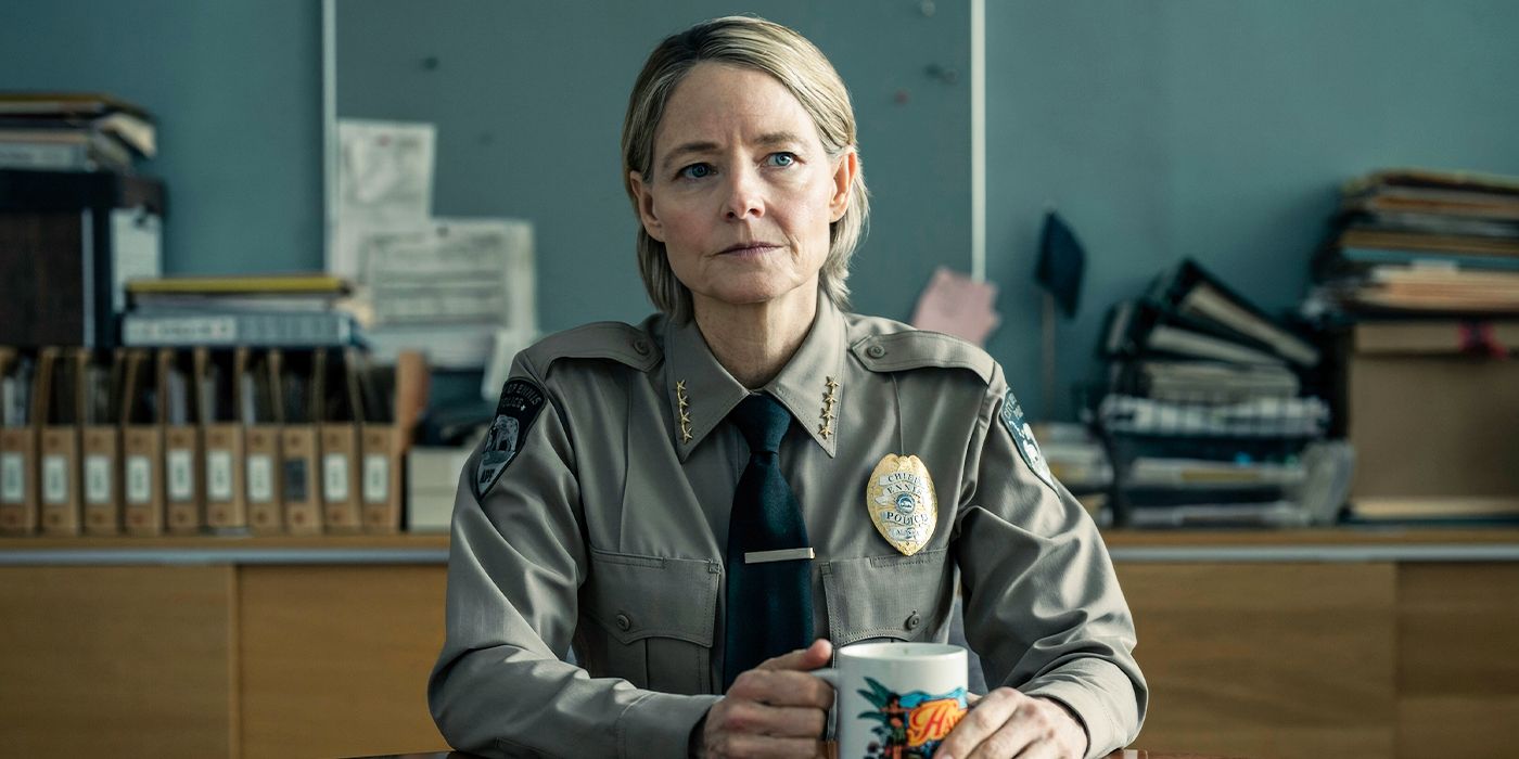 Jodie Foster as Liz Danvers sitting at a desk having a cup of coffee while wearing a police uniform in the True Detective: Night Country season finale. 