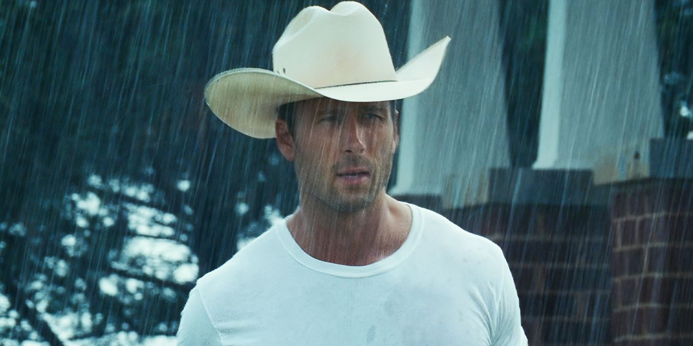 Glen Powell as Tyler Owens, walking in the rain while wearing a white cowboy hat and a t-shirt in Twisters.
