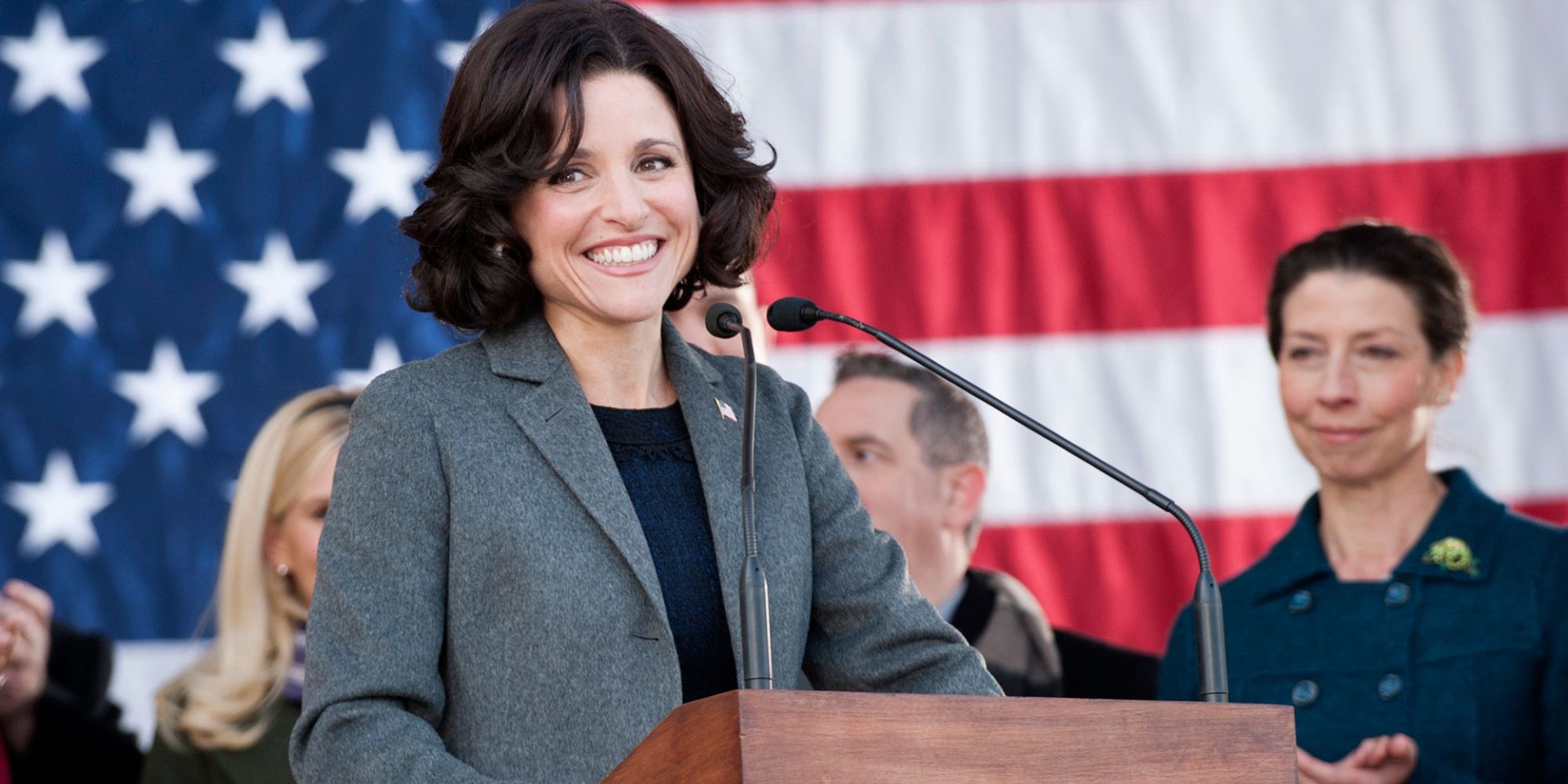 Julia Louis Drefyus as Selina Meyer standing at a podium with an American flag behind her in Veep