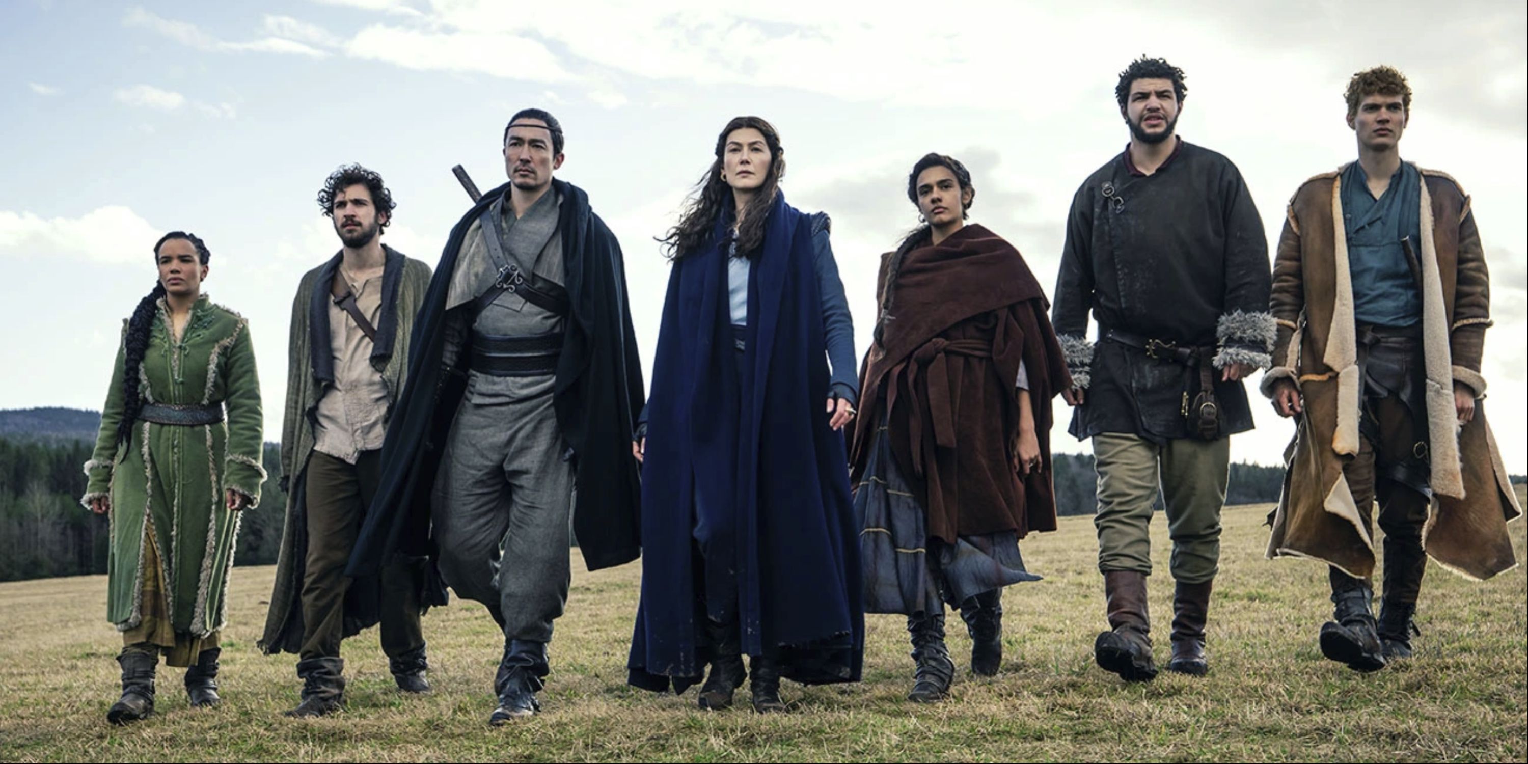 The cast of The Wheel of Time walking in a row in an open field.
