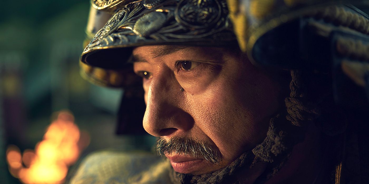 Hiroyuki Sanada as Yoshii Toranaga wearing armor and looking down with uncertainty as a fire blazes behind him in FX's Shōgun.