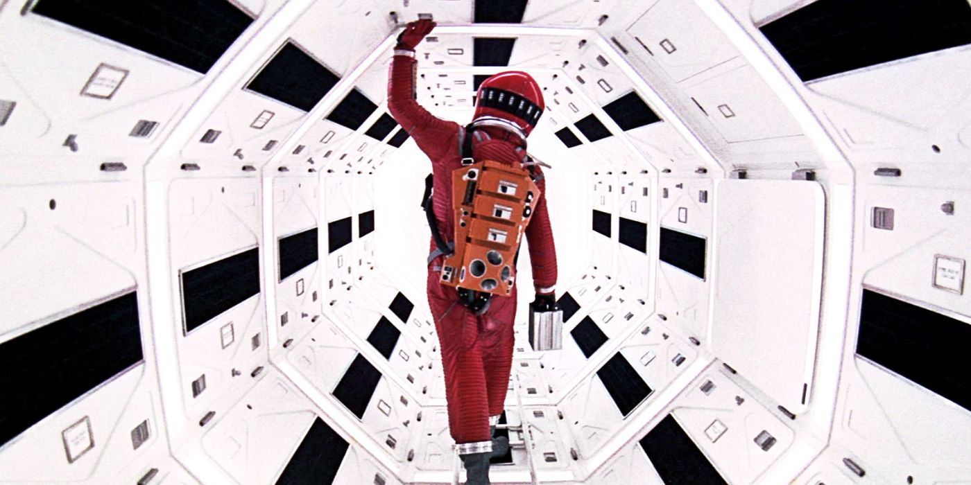 A red-suited astronaut walks down a white, brightly lit hallway aboard the space station in '2001: A Space Odyssey'