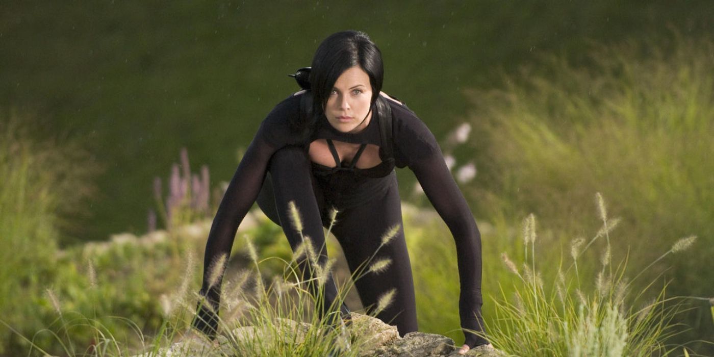 Charlize Theron wearing all black and crouching in the grass in Aeon Flux