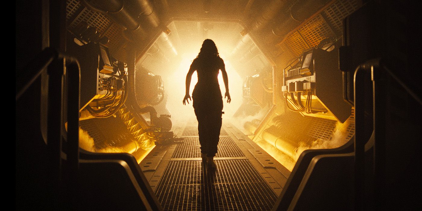A woman, seen from behind, in a dark corridor walks toward the light in Alien: Romulus