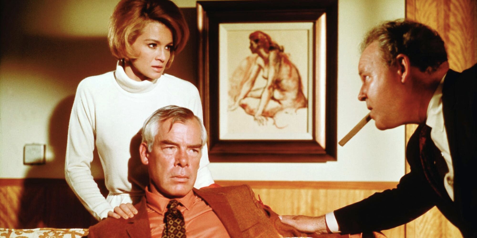 Angie Dickinson standing behind Lee Marvin sitting on a couch with Carroll O'Connor in their faces in Point Blank (1967)