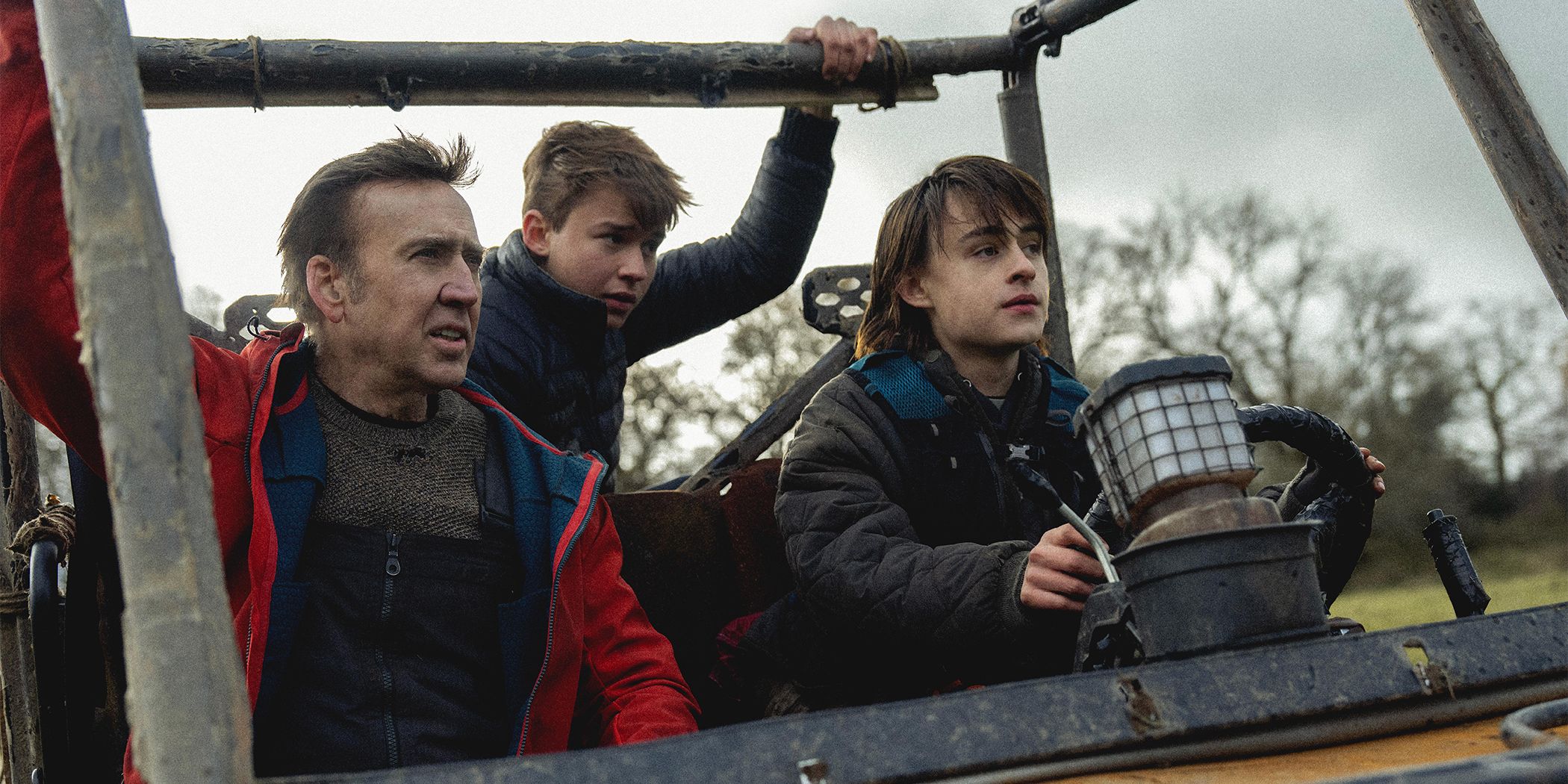 Nicolas Cage riding in an open vehicle with Jaeden Martell and Maxwell Jenkins
