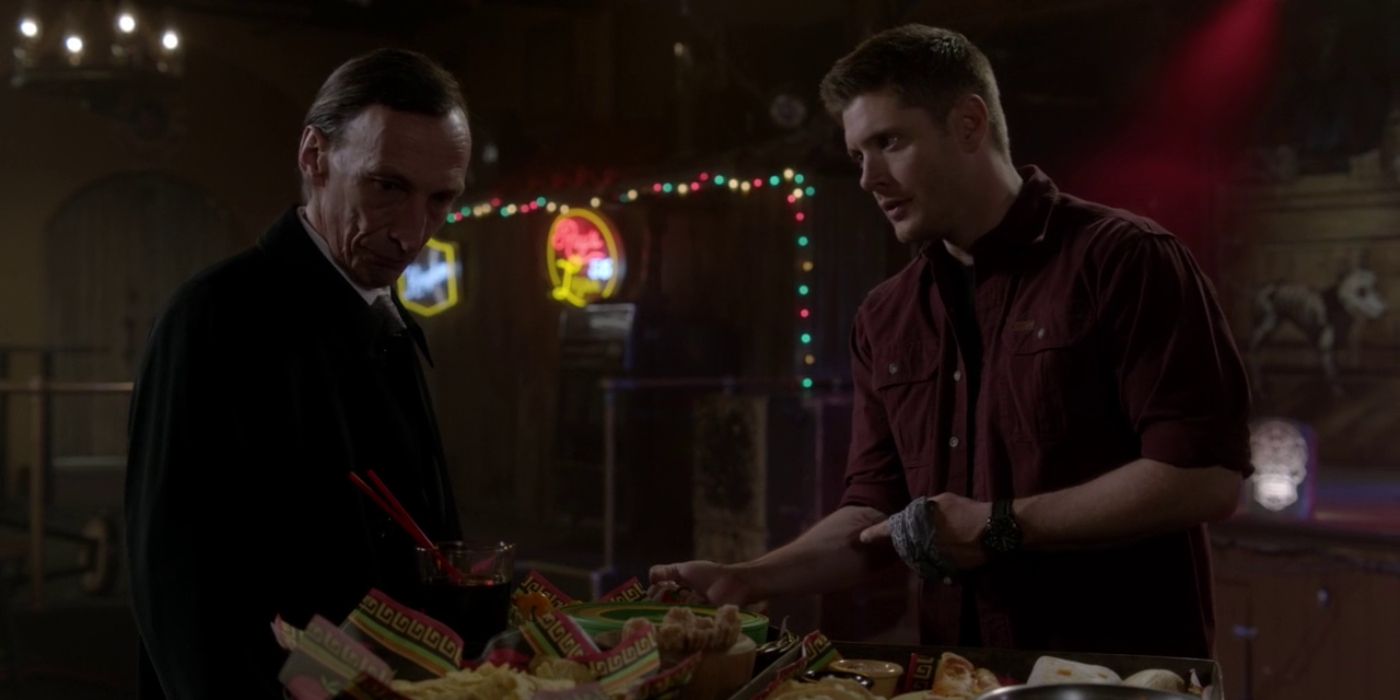 Dean Winchester points the to Mark of Cain on his arm as he talks to Death, who eyes off a feast of fatty food.