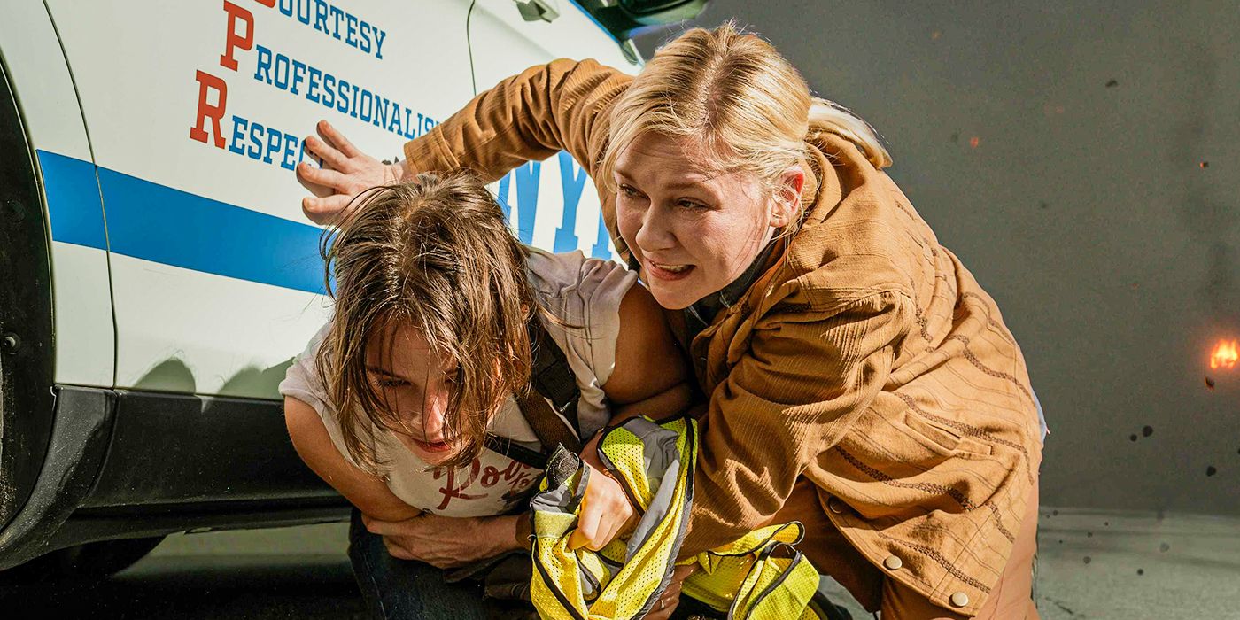 Kirsten Dunst as Lee and Cailee Spaeny as Jessie hiding from an explosion behind a police car in Civil War.