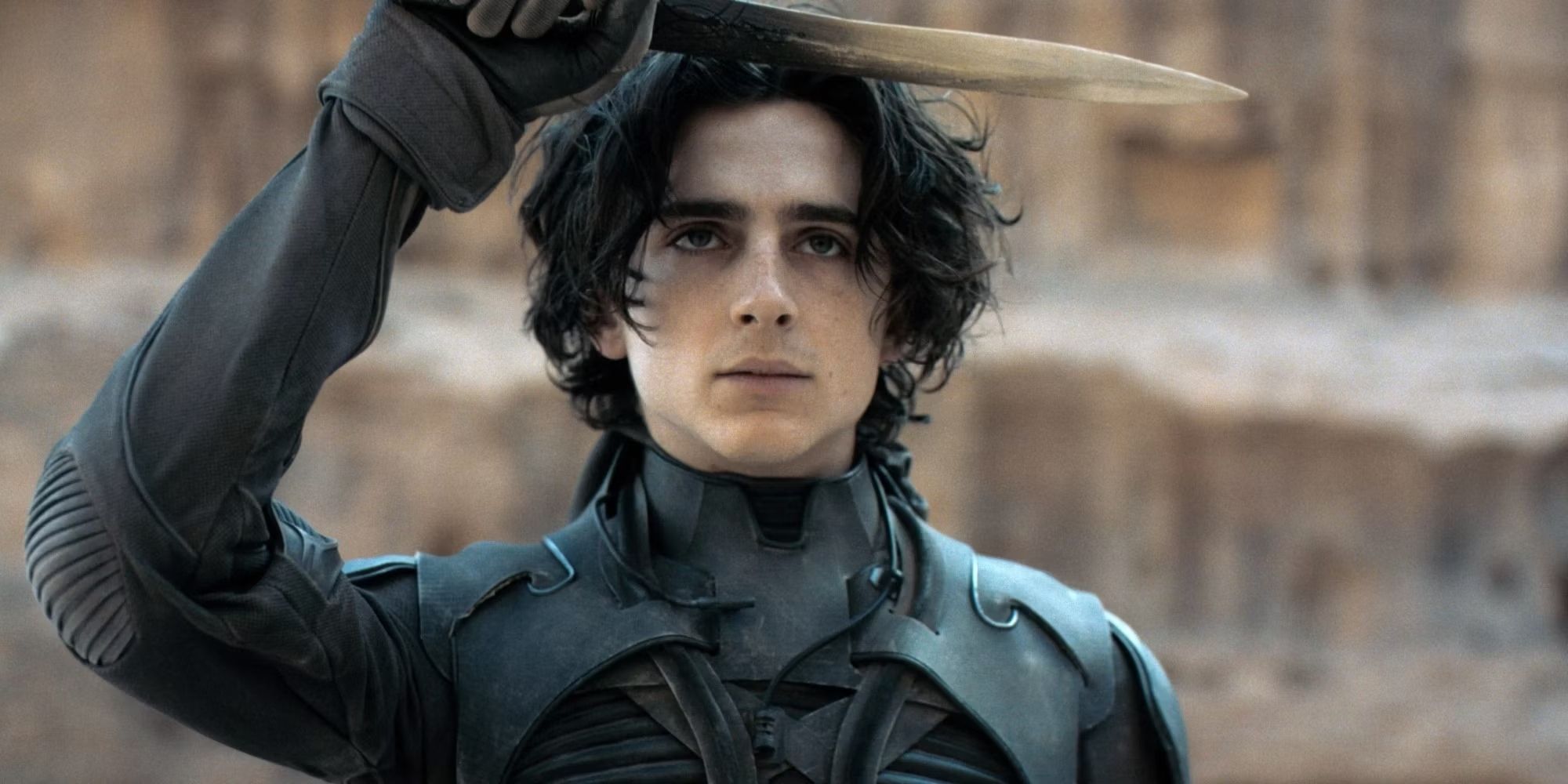 Timothée Chalamet as Paul Atreides, holding his knife over his head in Dune.