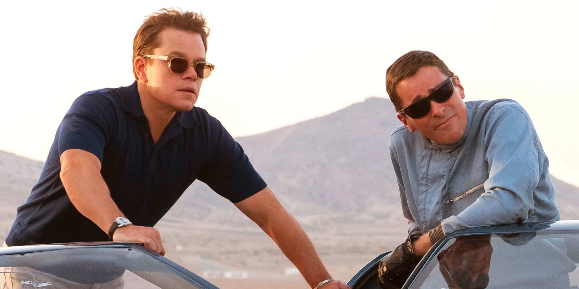 Matt Damon and Christian Bale hanging out next to a car in Ford v Ferrari.