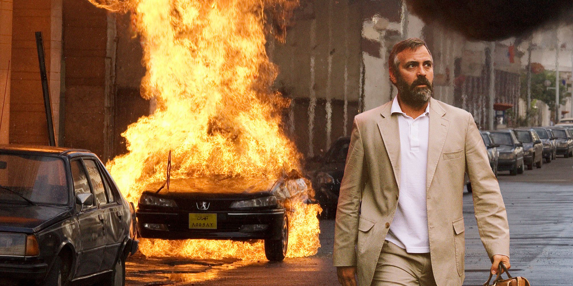 man in beige suit walking in front of a burning car