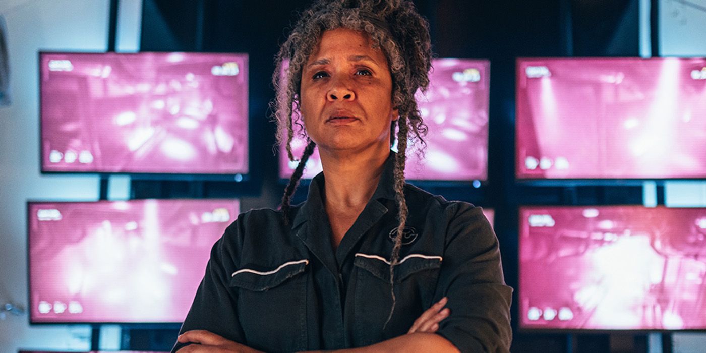 Golda Rosheuvel standing with her arms folded in front of several pink security monitors in Doctor Who