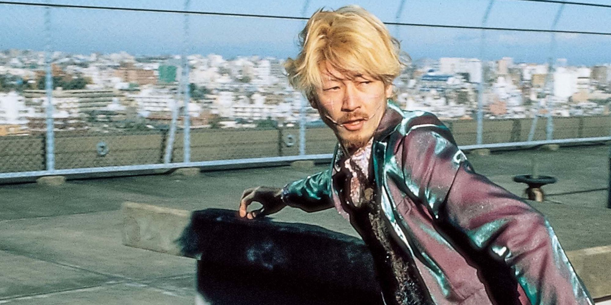 Tadanobu Asano wearing a shimmering shirt, running on a rooftop from something behind him
