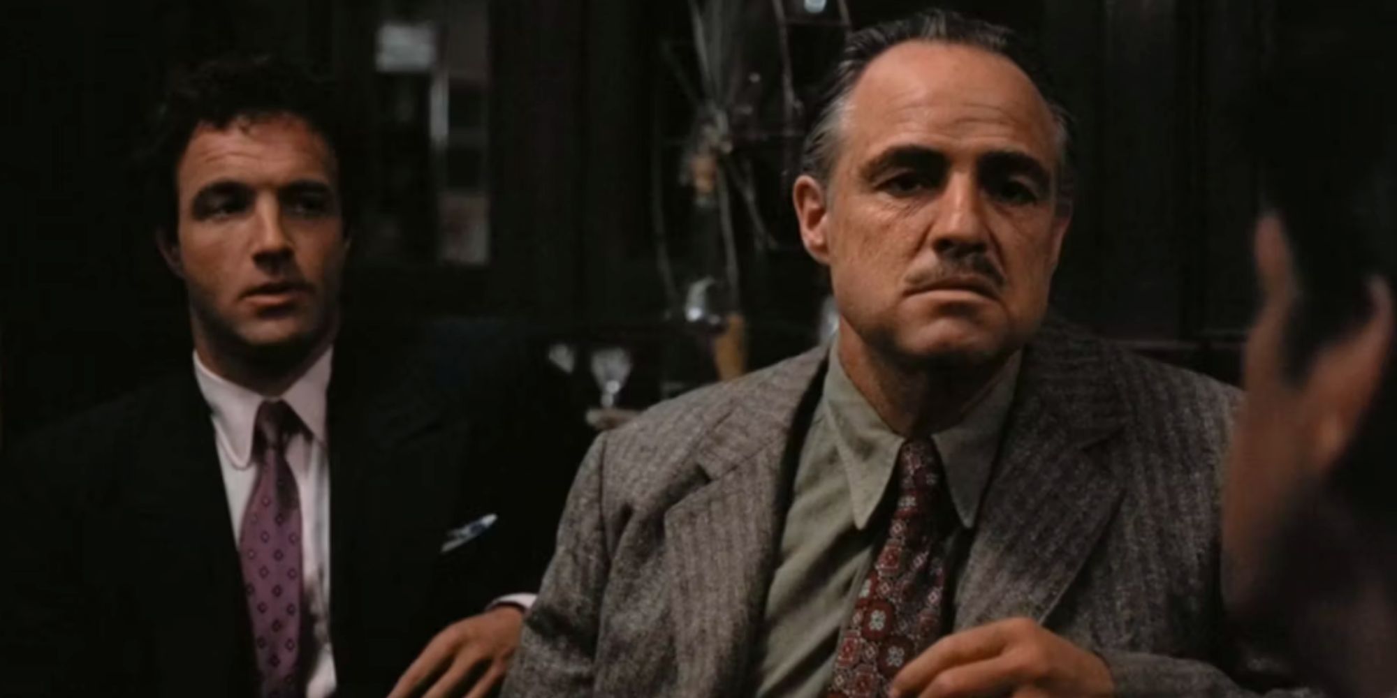 Sonny Corleone sitting next to Vito Corleone as he talks to another man in The Godfather (1972)