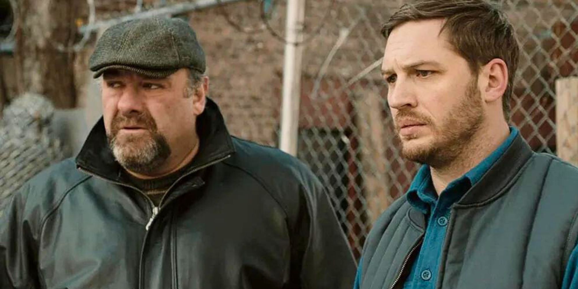 James Gandolfini as Marv standing next to Tom Hardy as Bob in front of a chain fence in The Drop (2014)