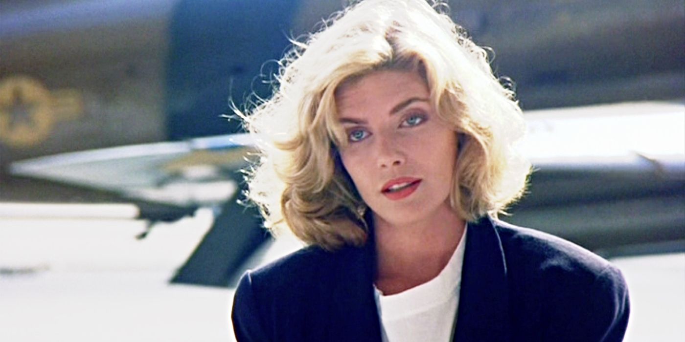 Kelly McGillis as Charlie, looking at someone offscreen with a plane behind her in Top Gun