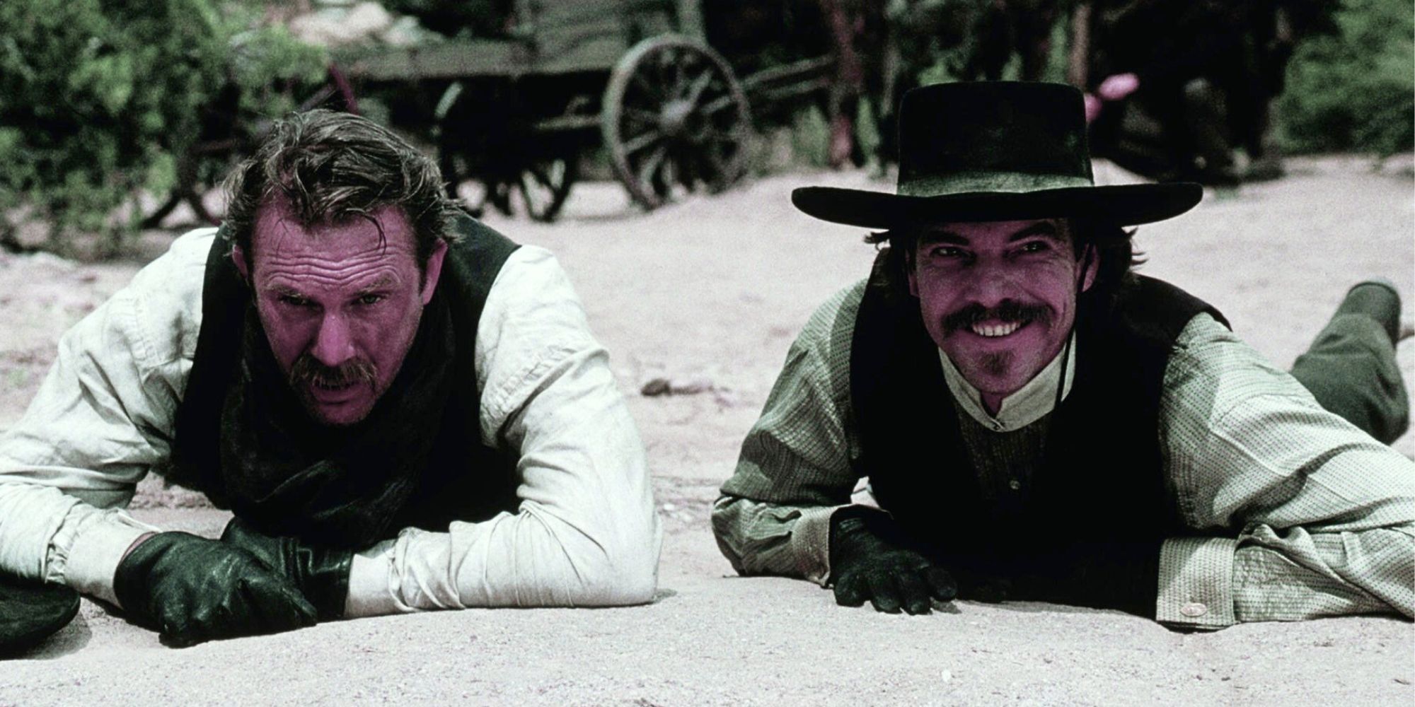 Kevin Costner and Dennis Quaid lying on the ground on their stomachs next to each other in Wyatt Earp (1994)