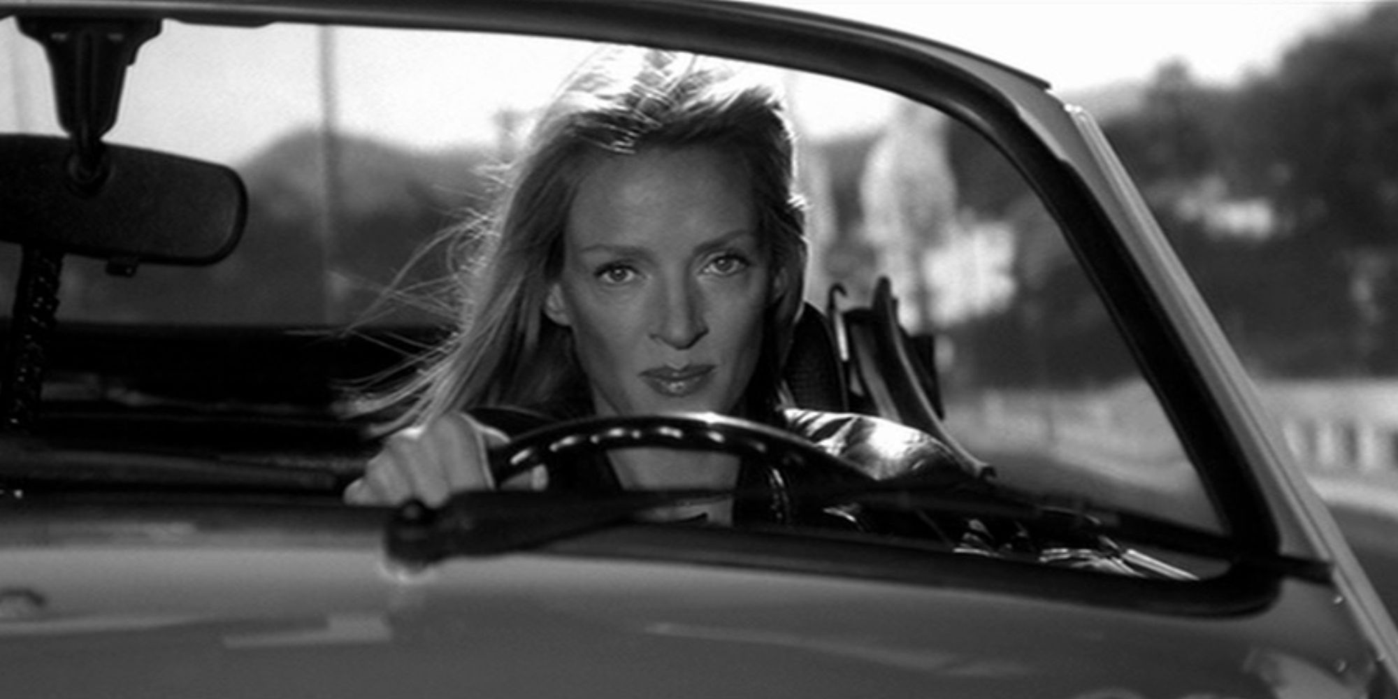 Uma Thurman as The Bride driving a car and smiling softly in black and white