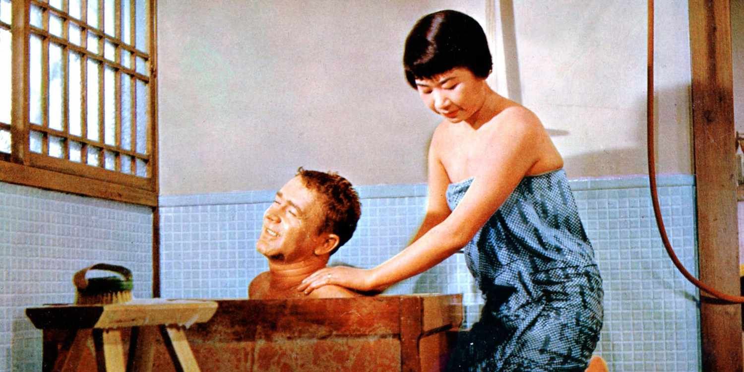 woman with towel around her body bathing a man in a wooden tub