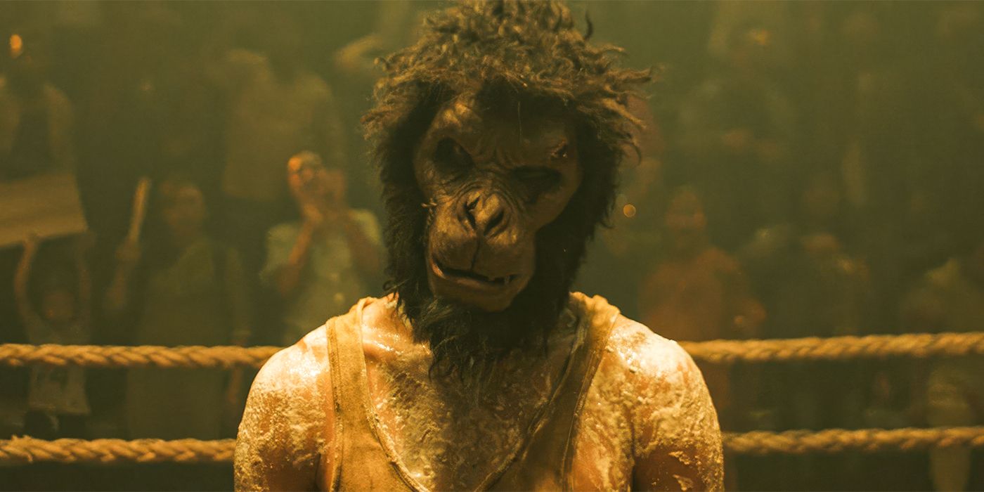Dev Patel wears a Monkey mask while looking into the camera in a boxing ring in Monkey Man